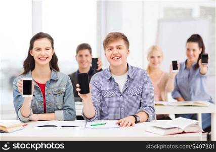 education, technology and internet - smiling students showing black blank smartphone screens at school
