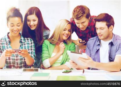education, technology and internet - students looking at smartphones and tablet pc