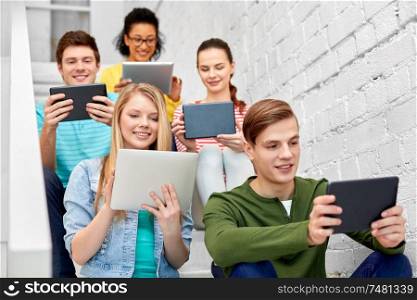 education, technology and learning concept - group of happy international high school students or classmates with tablet pc computers sitting on stairs. high school students with tablet computers