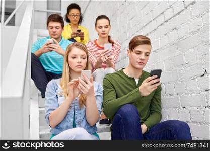 education, technology and learning concept - group of happy international high school students or classmates with smartphones sitting on stairs. students with smartphones sitting on stairs