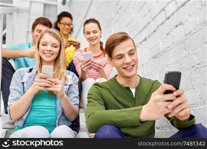 education, technology and learning concept - group of happy international high school students or classmates with smartphones sitting on stairs. students with smartphones sitting on stairs