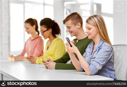 education, technology and learning concept - group of happy international high school students or classmates with smartphone in classroom. happy high school students with smartphones