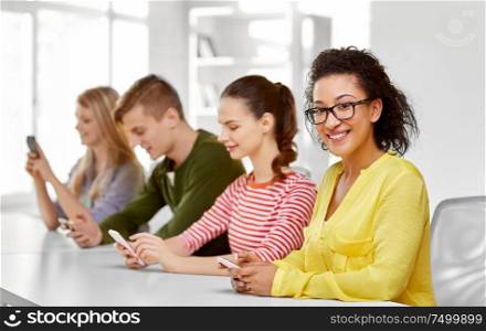 education, technology and learning concept - group of happy international high school students or classmates with smartphone in classroom. happy high school students with smartphones