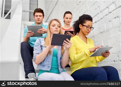 education, technology and learning concept - group of international high school students or classmates with tablet pc computers sitting on stairs. high school students with tablet computers