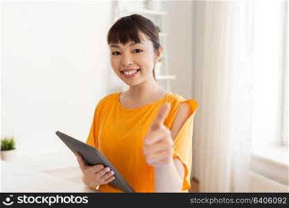 education, technology and people concept - happy smiling asian student girl with tablet pc computer learning at home showing thumbs up. student with tablet pc showing thumbs up at home