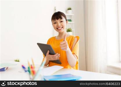 education, technology and people concept - happy smiling asian student girl with tablet pc computer learning at home showing thumbs up. student with tablet pc showing thumbs up at home