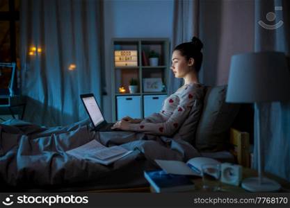 education, technology and people concept - teenage student girl with laptop computer learning in bed at home at night. teenage girl with laptop learning in bed at night