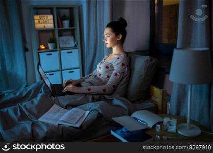 education, technology and people concept - teenage student girl with laptop computer learning in bed at home at night. teenage girl with laptop learning in bed at night