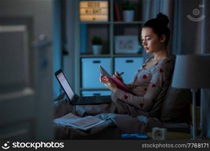 education, technology and people concept - teenage student girl with notebook and laptop computer learning in bed at home at night. student girl with notebook and laptop at night
