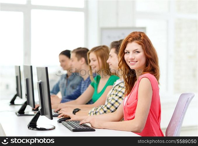 education, technology and school concept - smiling female student with classmates in computer class at school