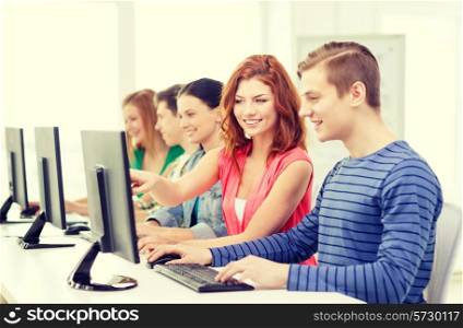 education, technology and school concept - smiling female student with classmates in computer class at school