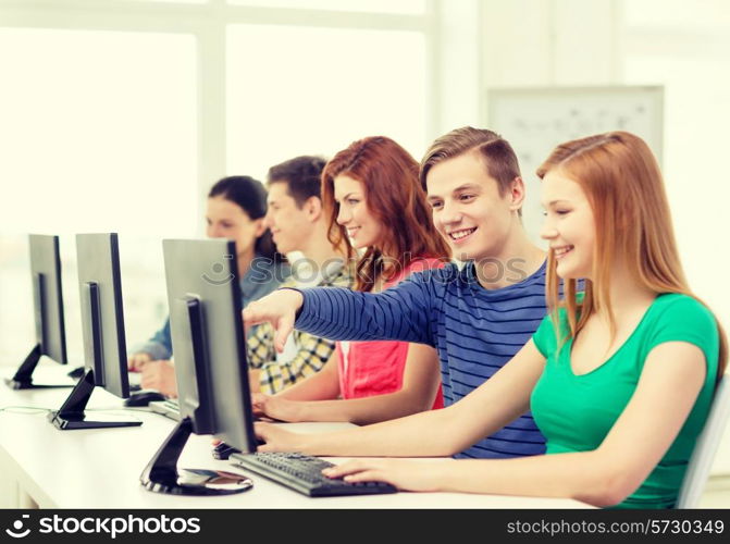 education, technology and school concept - smiling female student with classmates in computer class at school