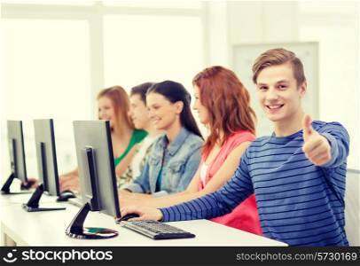 education, technology and school concept - smiling male student with classmates in computer class at school showing thumbs up
