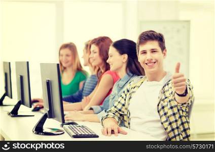 education, technology and school concept - smiling male student with classmates in computer class at school showing thumbs up