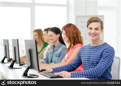 education, technology and school concept - smiling male student with classmates in computer class