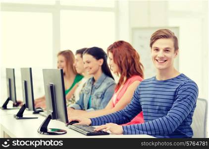 education, technology and school concept - smiling male student with classmates in computer class