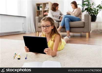 education, technology and school concept - student girl with tablet computer lying on floor and doing homework. girl with tablet computer lying on floor at home