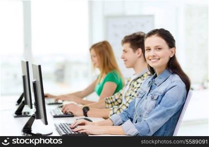 education, technology and school concept - three smiling students in computer class