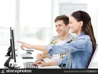 education, technology and school concept - two smiling students in computer class, girl pointing finger at screen