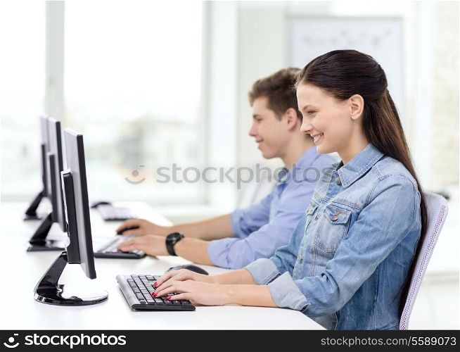 education, technology and school concept - two smiling students in computer class