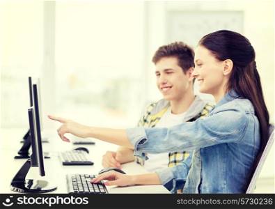 education, technology and school concept - two smiling students in computer class, girl pointing finger at screen