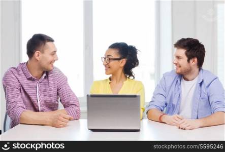 education, technology, business, startup and office concept - three smiling colleagues with laptop in office