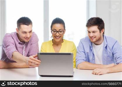 education, technology, business, startup and office concept - three smiling colleagues with laptop in office