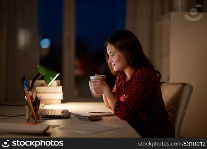 education, technology, freelance, overwork and people concept - woman or student girl with laptop computer drinking coffee at night home. student woman with laptop and coffee at night home