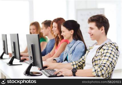 education, technology, friendship and school concept - smiling male student with classmates in computer class