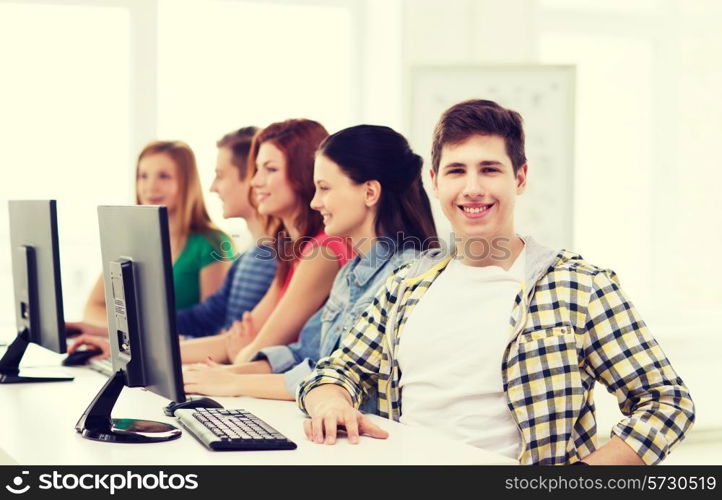 education, technology, friendship and school concept - smiling male student with classmates in computer class