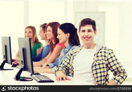 education, technology, friendship and school concept - smiling male student with classmates in computer class