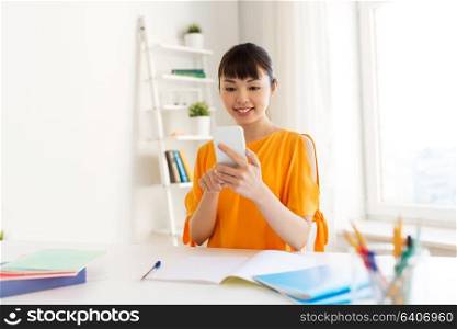education, technology, learning and people concept - happy asian student girl with book and notebooks using smartphone at home. student girl learning and using smartphone at home