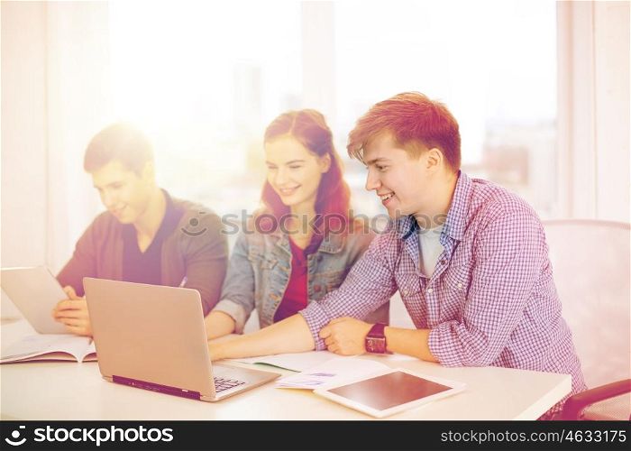 education, technology, school and internet concept - three smiling students with laptop, tablet pc and notebooks at school