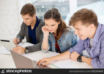 education, technology, school and internet concept - three smiling students with laptop, tablet pc and notebooks at school