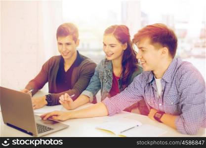 education, technology, school and internet concept - three smiling students with laptop and notebooks at school