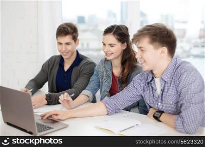 education, technology, school and internet concept - three smiling students with laptop and notebooks at school