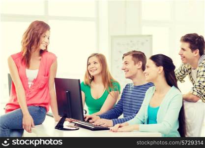 education, technology, school and people concept - group of smiling students having discussion in computer class at school