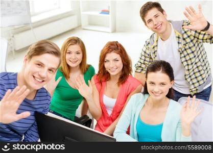 education, technology, school and people concept - group of smiling students waving hands in computer class at school