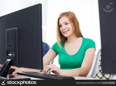 education, technology, school and people concept - smiling female student in computer class at school