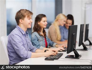 education, techology and internet concept - group of smiling students looking at computer monitor at school