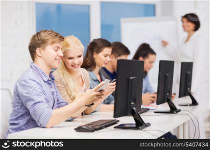 education, techology and internet concept - group of smiling students with computer monitor and smartphones at school
