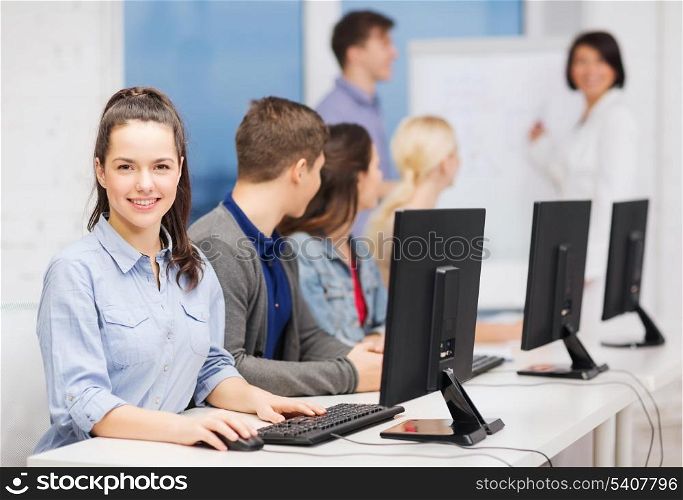 education, techology and internet concept - group of smiling students with computer monitor looking at teacher at school