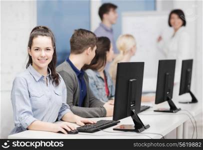education, techology and internet concept - group of smiling students with computer monitor looking at teacher at school