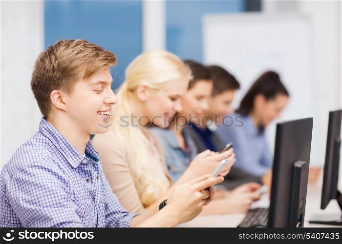 education, techology and internet concept - group of smiling students with computer monitor and smartphones