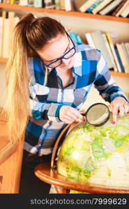 Education travel and geography concept. Young clever woman female student in blue glasses in library with globe and magnifying glass