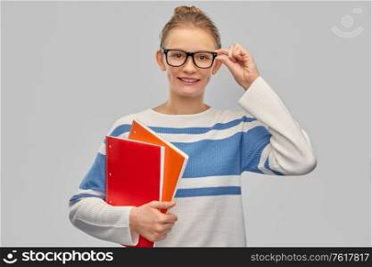 education, travel and tourism concept - happy smiling teenage student girl in glasses with notebooks over grey background. happy smiling teenage student girl with notebooks