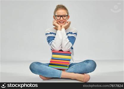 education, travel and tourism concept - happy smiling teenage student girl in glasses with books sitting on floor over grey background. happy smiling teenage student girl with books