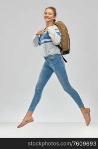 education, travel and tourism concept - happy smiling teenage student girl with school bag or backpack jumping over grey background. happy teenage student girl with school bag jumping