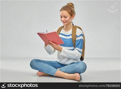 education, travel and tourism concept - happy smiling teenage student girl with school bag or backpack and notebook sitting on floor over grey background. teenage student girl with school bag and notebook