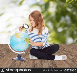 education, travel, childhood, geography and school concept - happy little student girl looking at globe with magnifier over green background